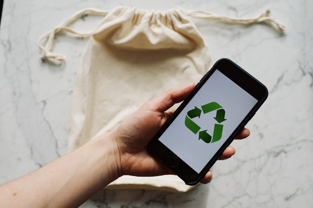 recyclable bag in back someone holding iphone with recycle symbol