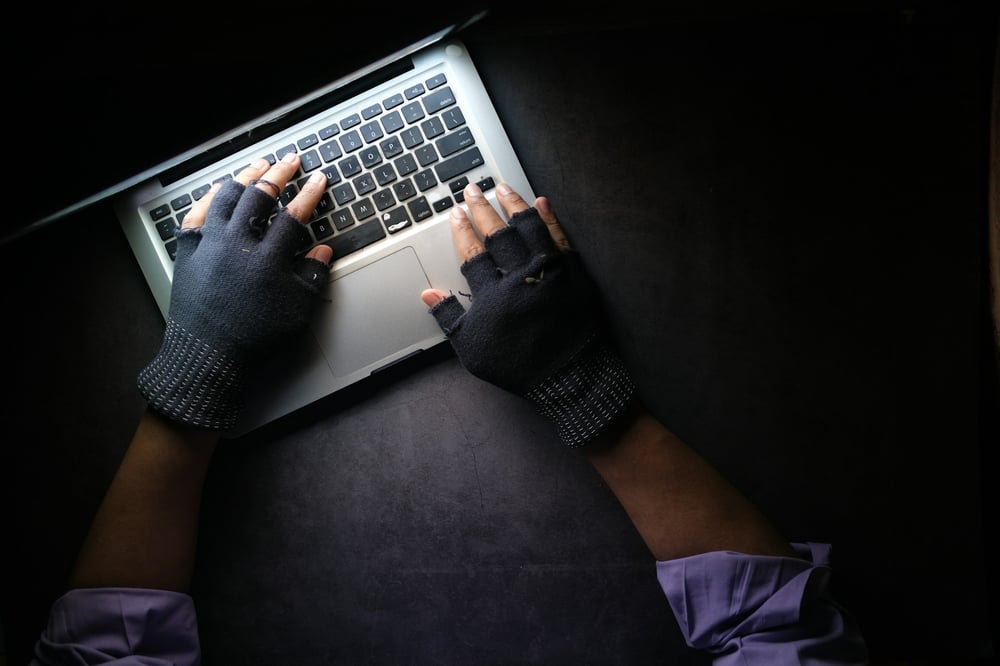 hands wearing fingerless gloves typing on a laptop keyboard